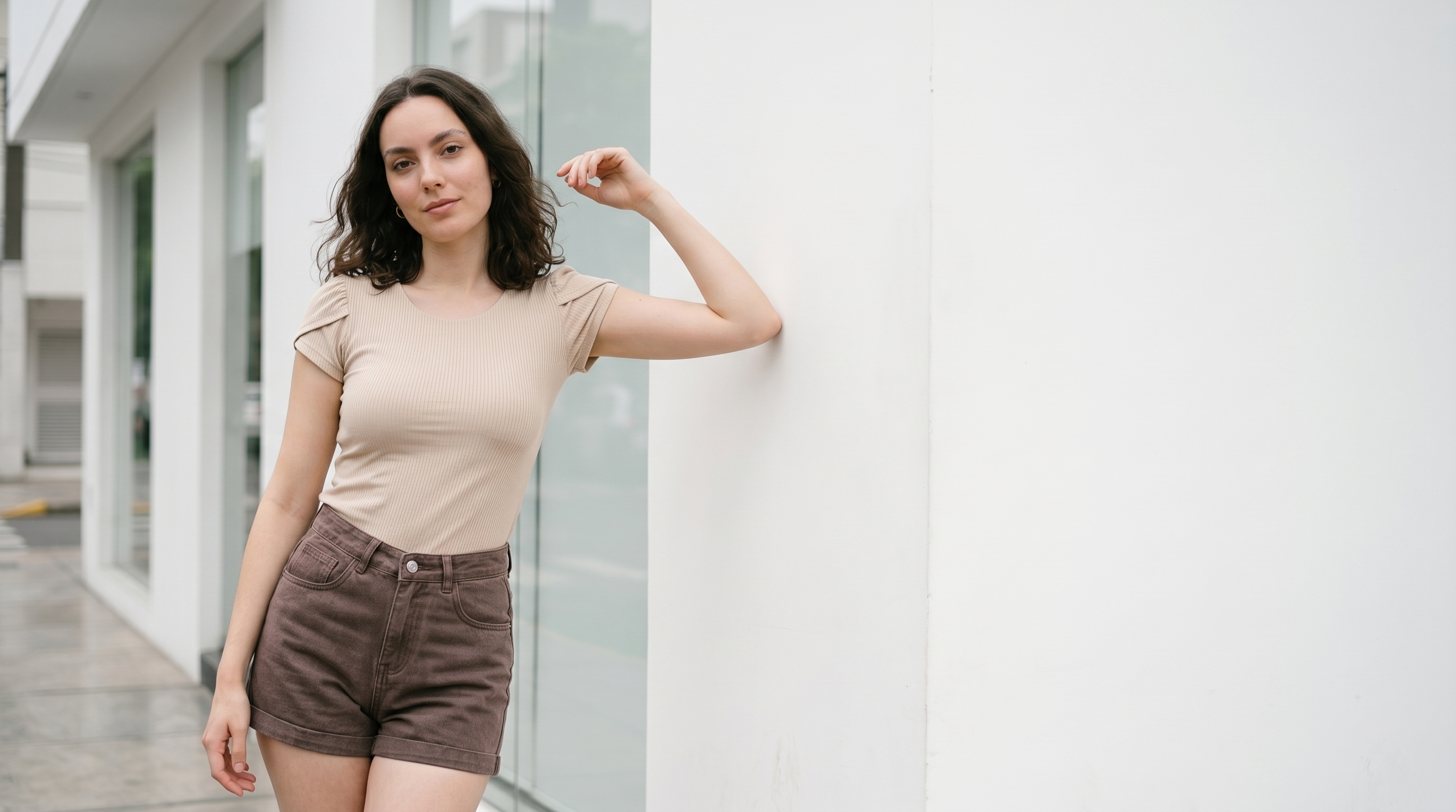Modelo con top acanalado beige apoyada en pared blanca